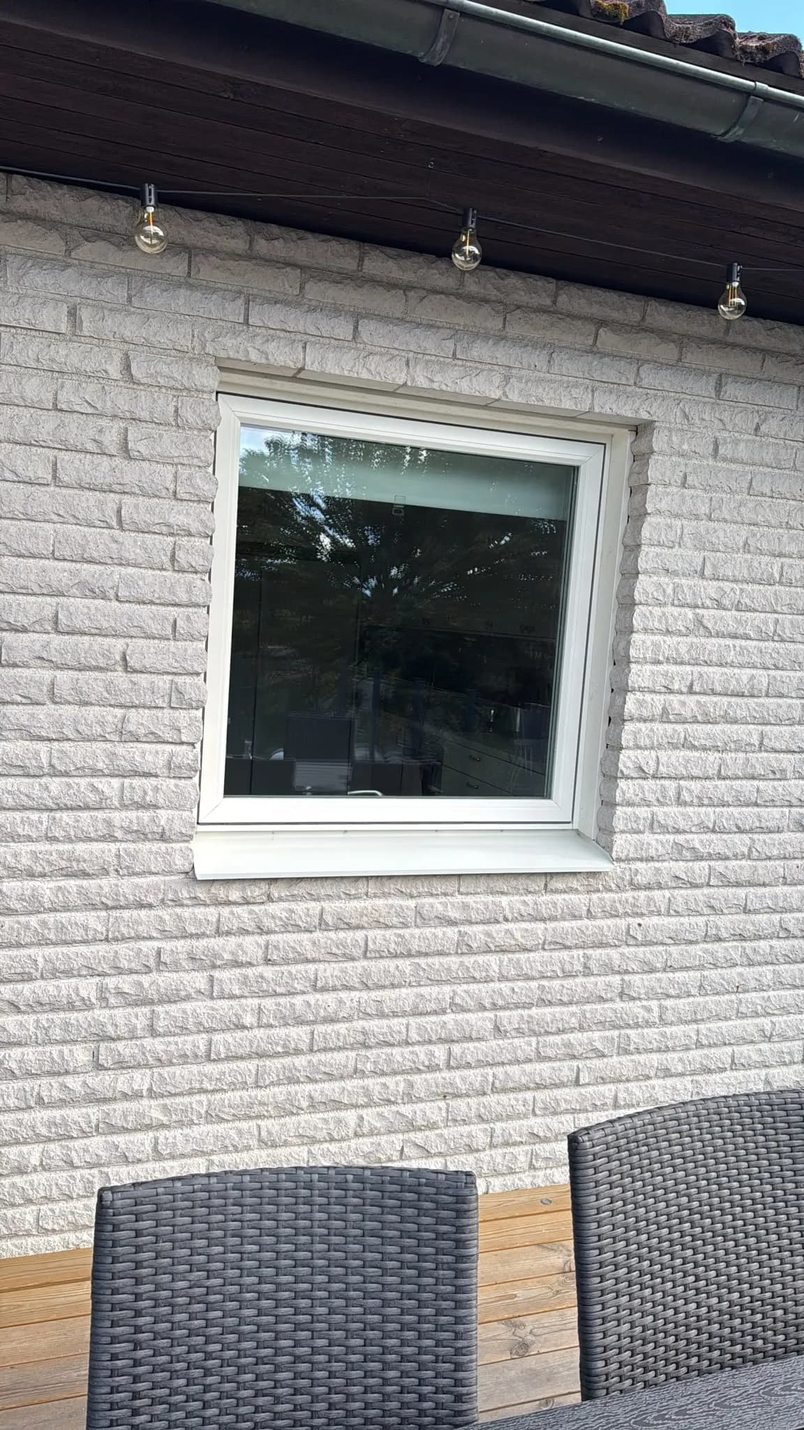 Nytt vitt fönster i fasad av vitt tegel, sett från altanen med utemöbler i förgrunden.