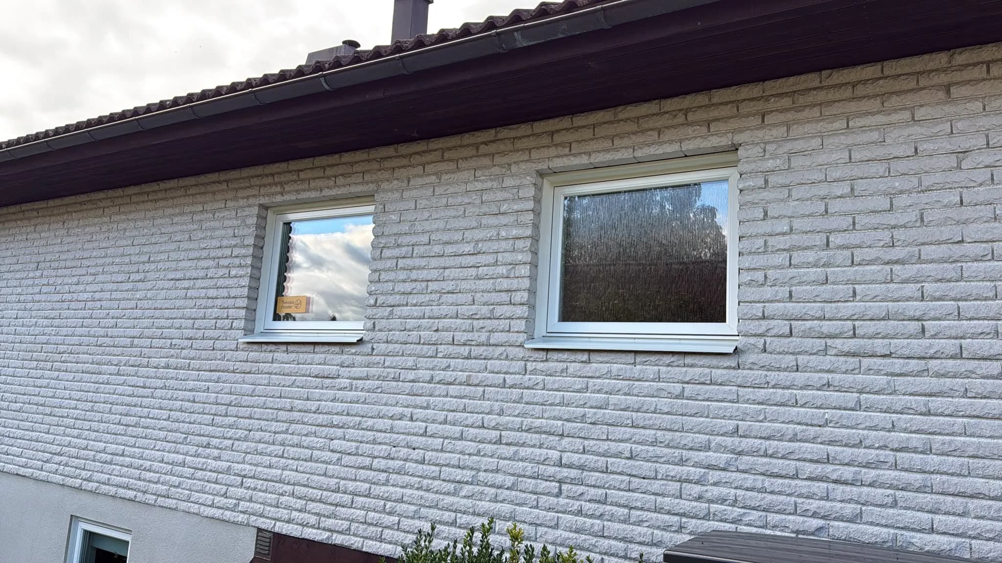 Fasad i vitt tegel med två nya fönster, det högra med ornamentglas mot insyn.