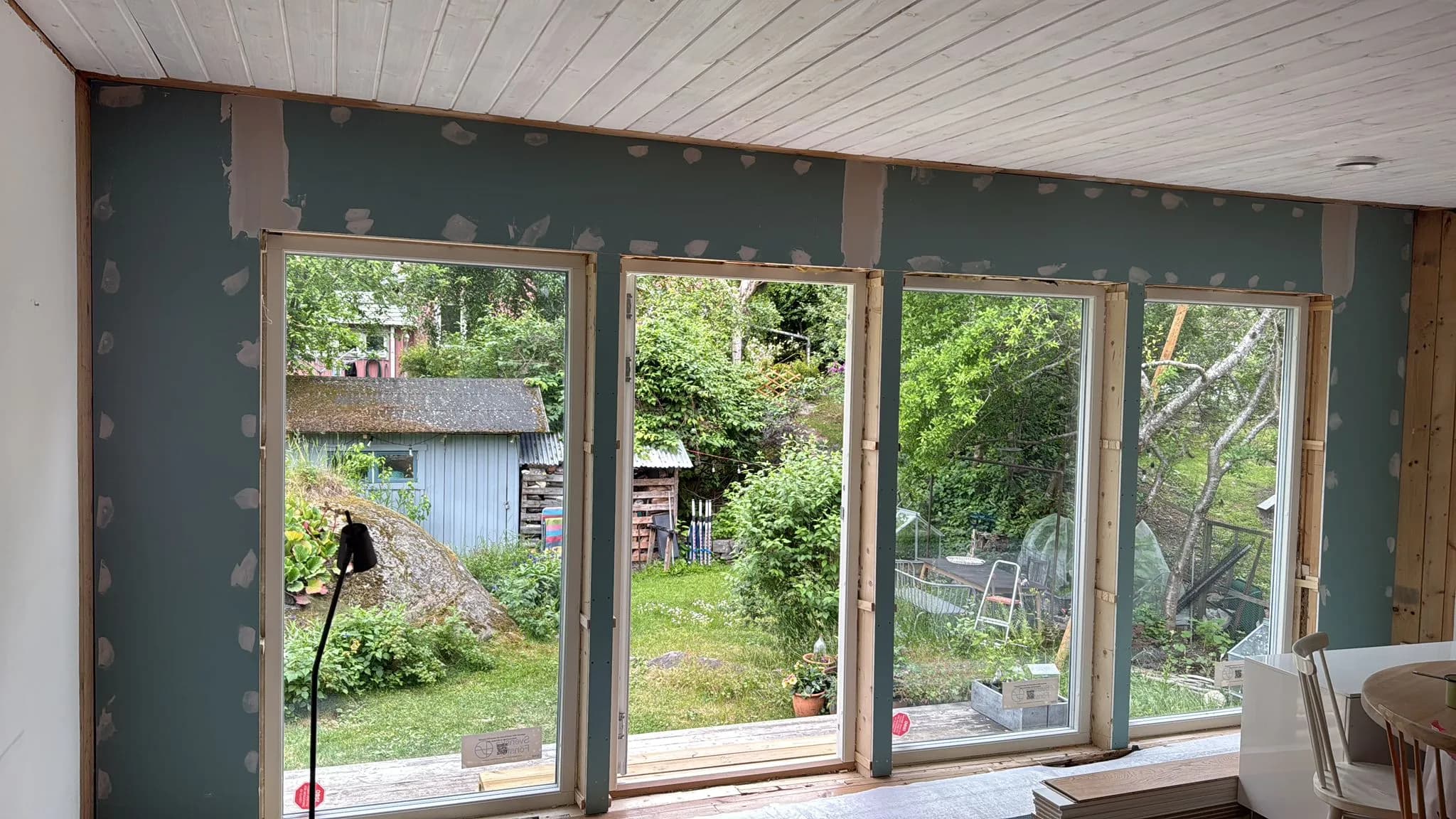 Nya fönster och fönsterdörr inifrån, väggen klädd med gröna gipsskivor och spacklade skruvhål innan smygarna gjorts.