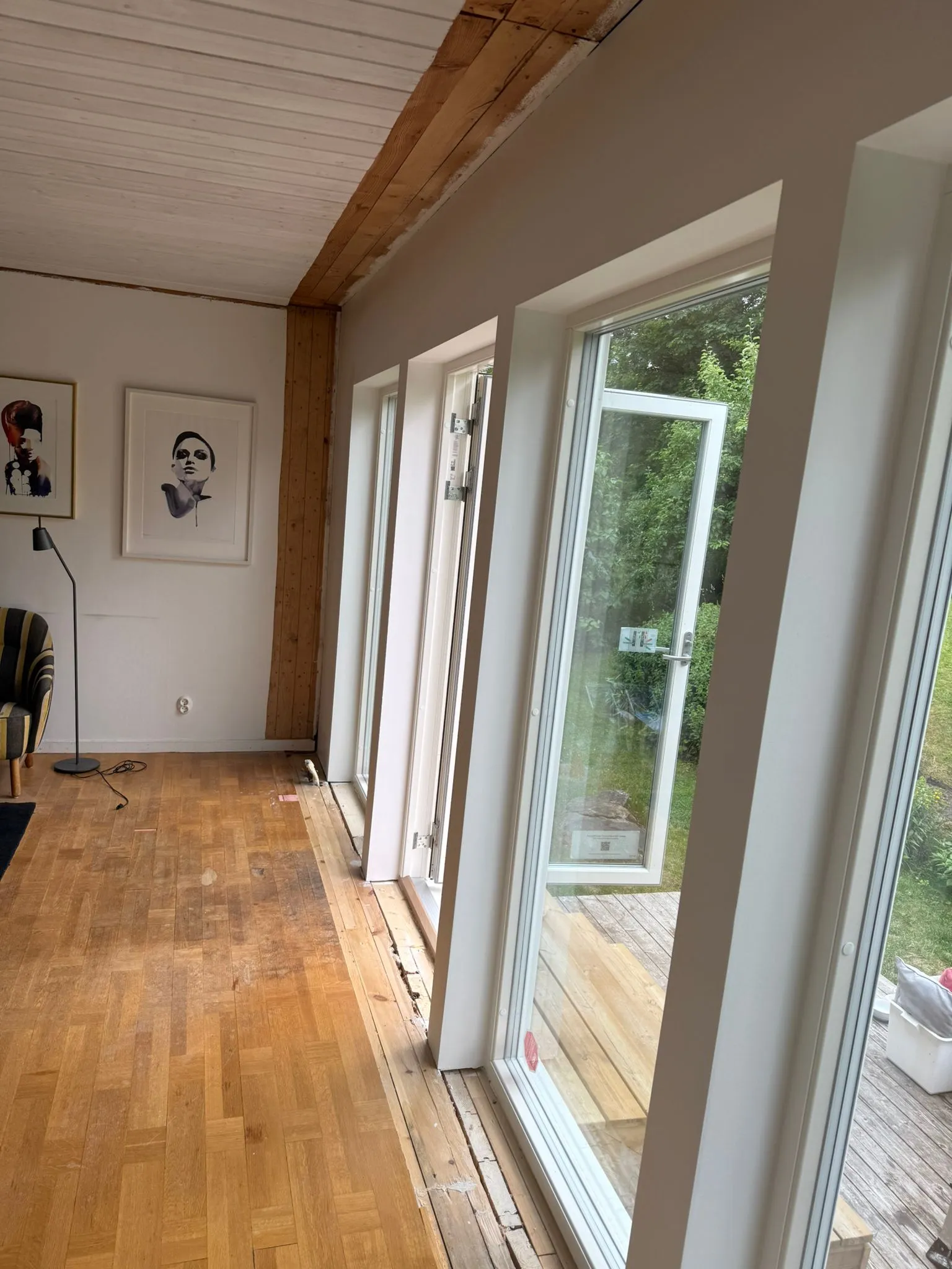 Fönsterdörr öppen utåt bredvid fasta glaspartier med djupa vita smygar, sett snett inifrån vardagsrummet.