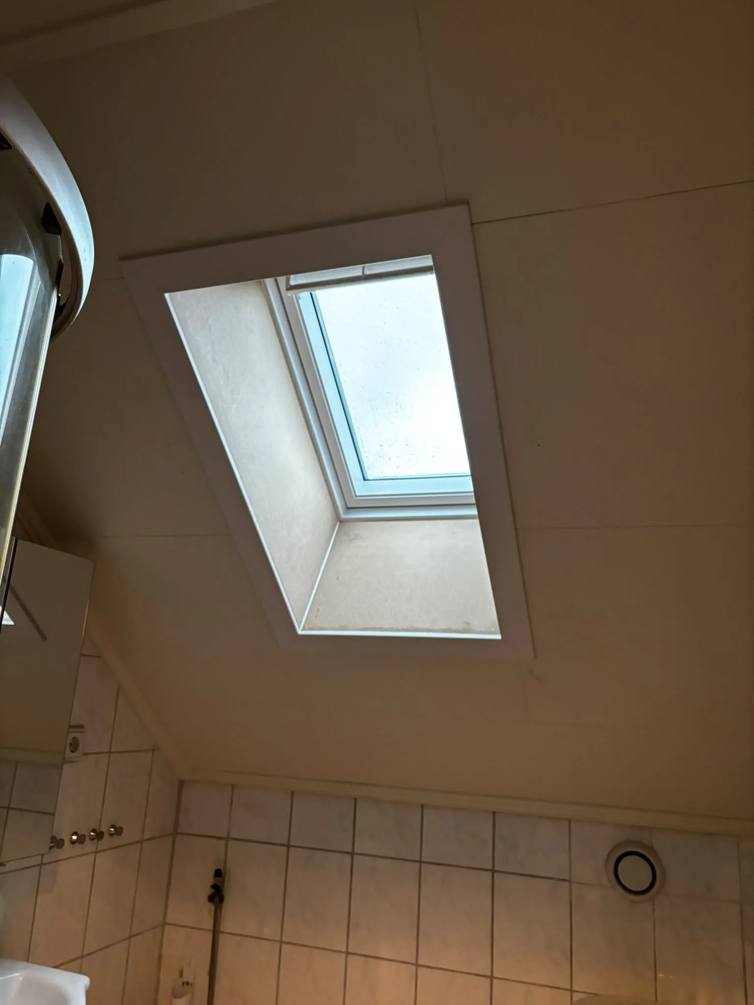 Takfönster i badrummets sneda tak, smygen ännu omålad, med kakelvägg och duschkabin nedanför.