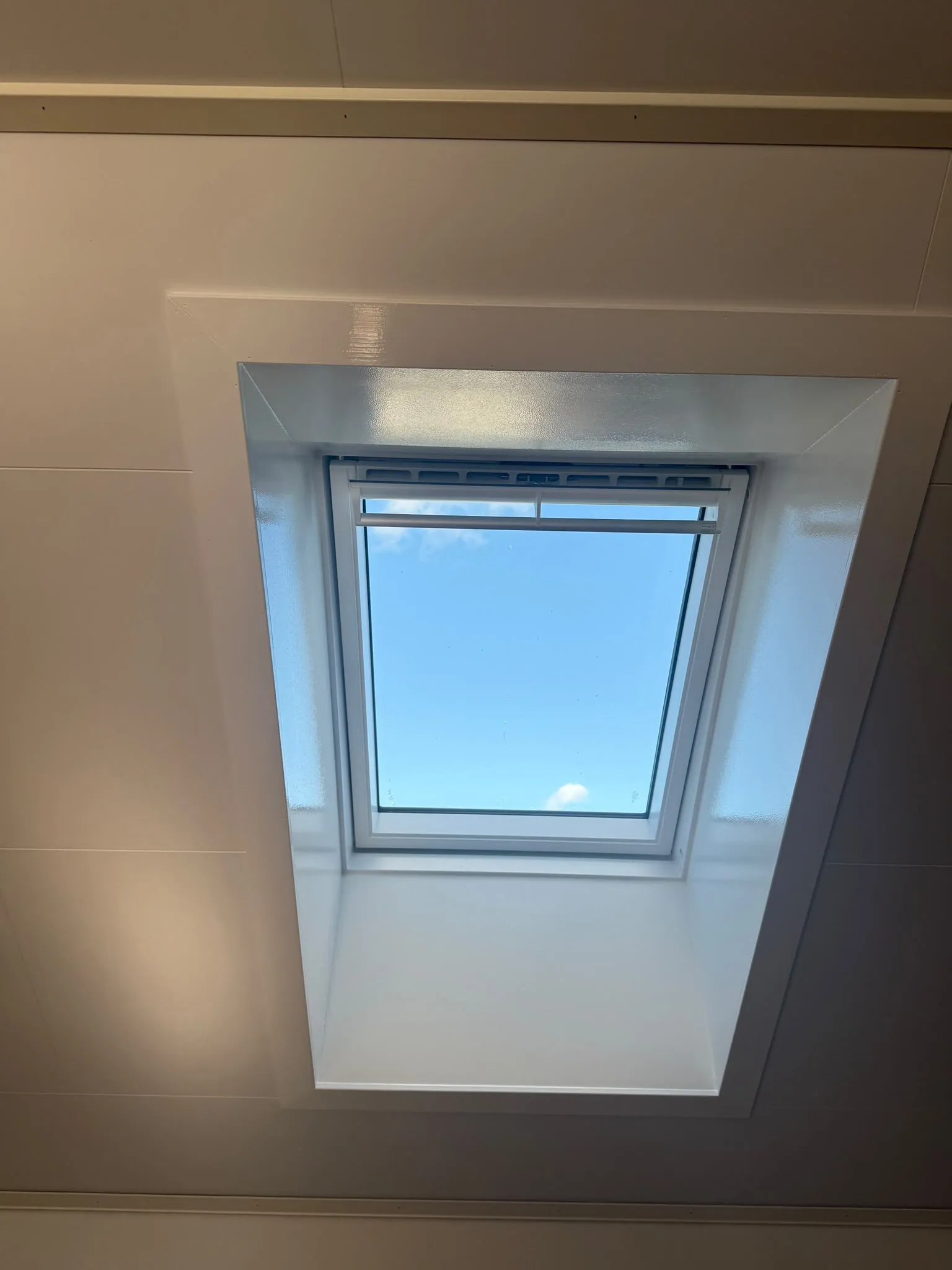Nytt VELUX-takfönster i snett innertak, med vitmålad smyg och blå himmel genom glaset.