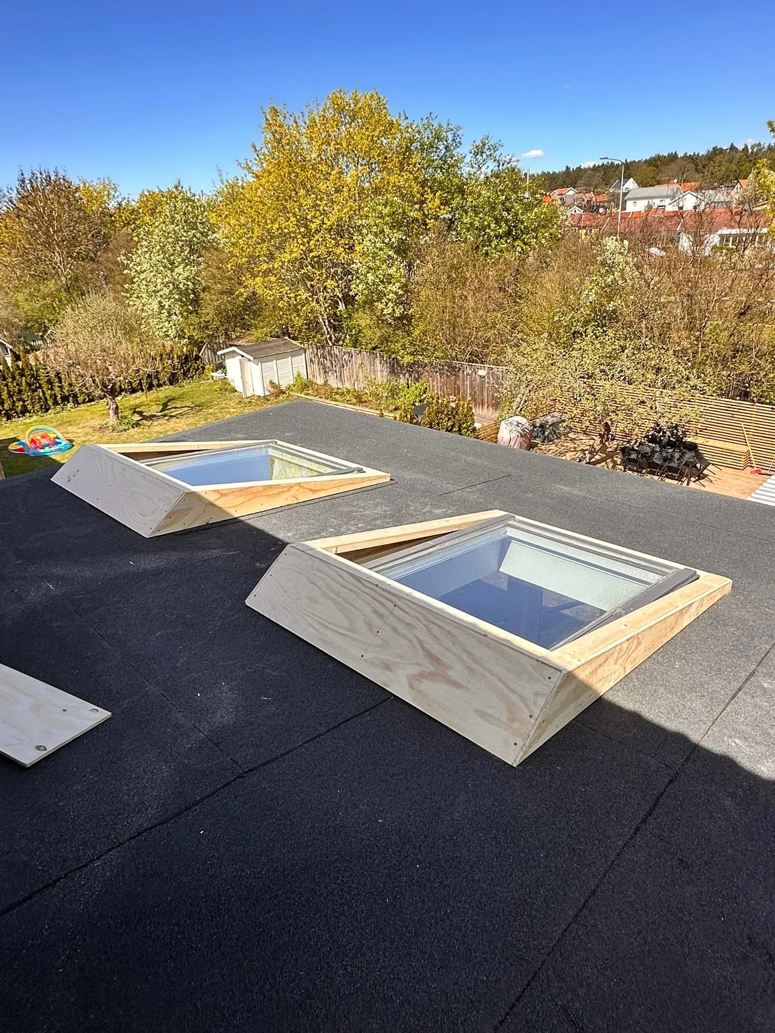 Två Velux takfönster på platt papptak, monterade på nya plywoodklädda ramverk som ger dem större lutning.