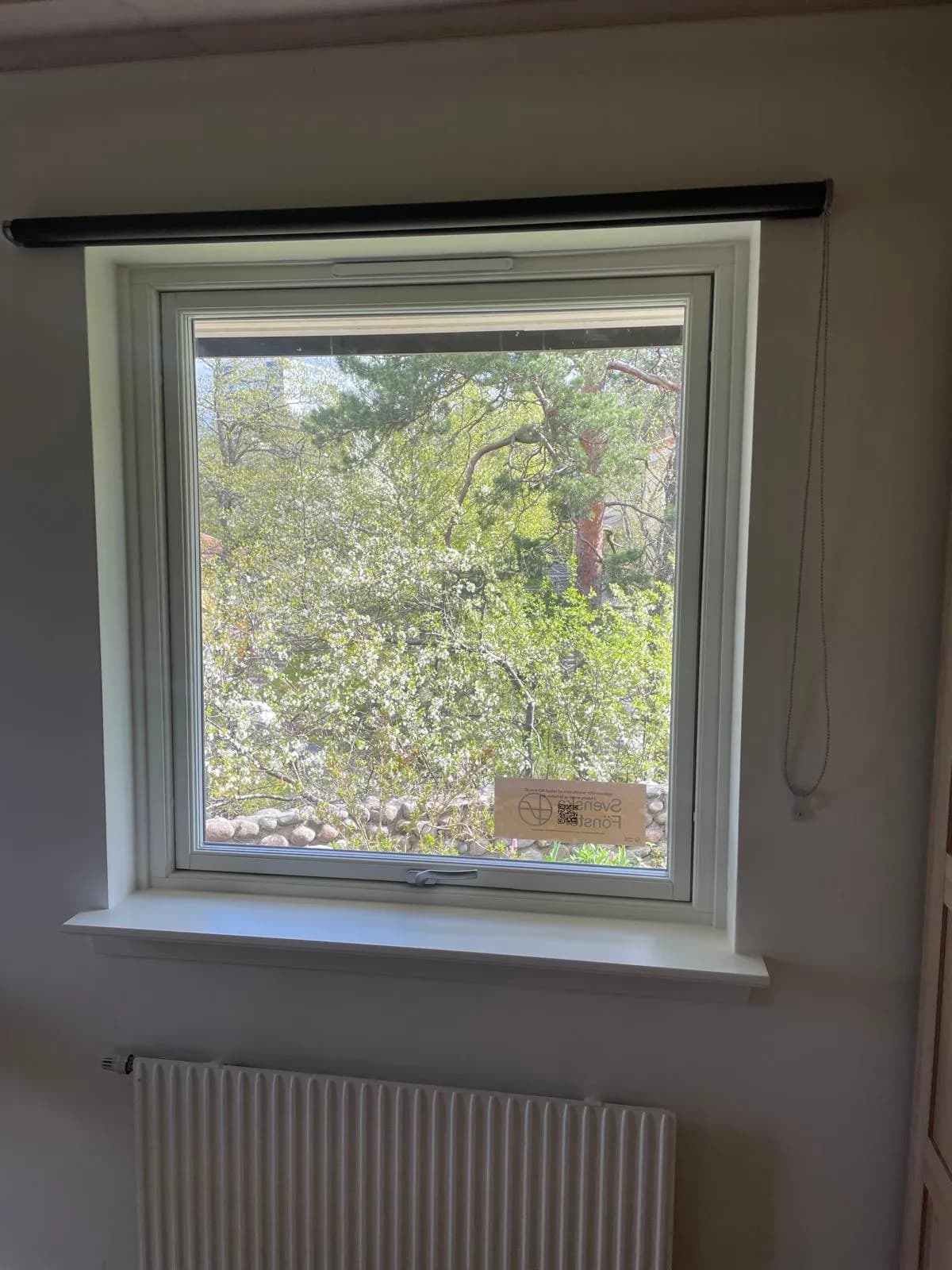 Nytt vitt fönster inifrån med släta spacklade smygar, vit fönsterbänk och radiator under, utsikt mot blommande trädgård.